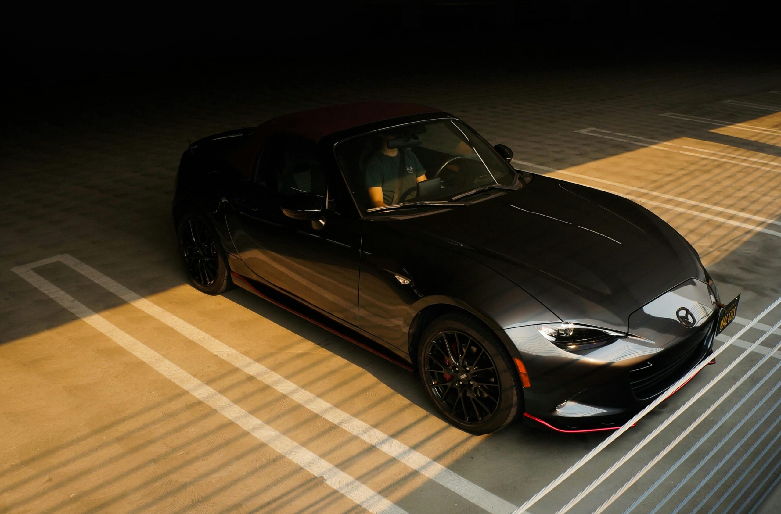 Black Mazda MX-5 sports car parked in a sunlit parking lot, showcasing elegance and style.